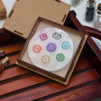 Round selenite crystal plate engraved with colorful chakra symbols in wooden box on wooden surface