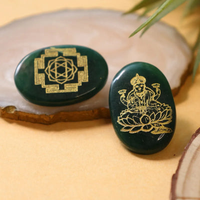 Two dark green oval stones with golden engravings, one of Lakshmi goddess and one geometric pattern, on wooden slices