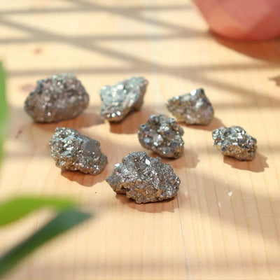 Seven shiny raw pyrite mineral stones on a light wooden surface with soft natural lighting