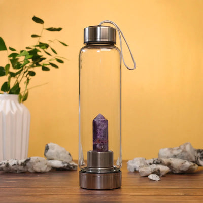 Glass water bottle with metal lid and amethyst crystal inside on wooden table with yellow background