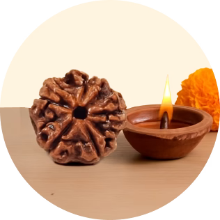 Close-up of a single eight-faced Rudraksha bead next to a lit clay oil lamp and an orange marigold flower