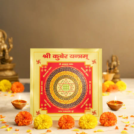 Shri Kubera Yantra sacred diagram in red and gold with marigold flowers and oil lamps on a white surface