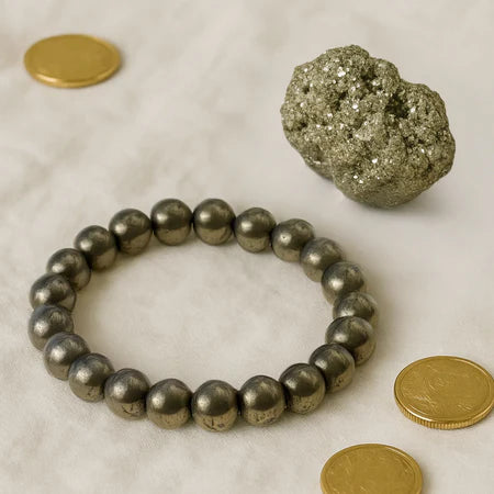 Pyrite mineral cluster and polished pyrite bead bracelet on white surface with gold coins