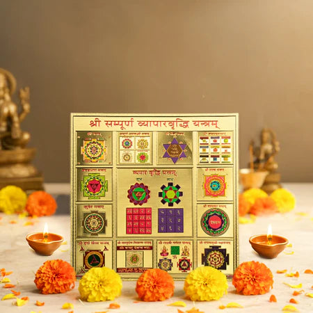 Golden Shri Sampoorna Vyapar Vriddhi Yantra with sacred symbols, surrounded by marigold flowers and lit oil lamps