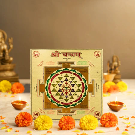 Shri Yantra sacred geometric diagram surrounded by lit oil lamps and marigold flowers on a white cloth