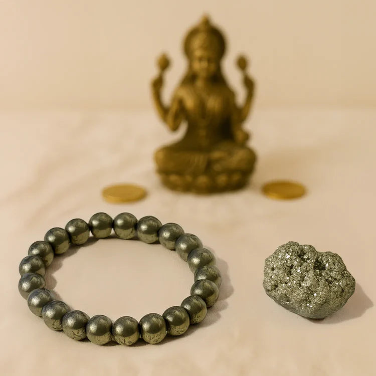 Pyrite bead bracelet, raw pyrite stone, and bronze Hindu deity statue on beige cloth background