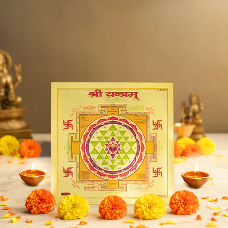 Sri Yantra sacred geometric diagram on yellow card surrounded by marigold flowers and lit diyas in a spiritual setting